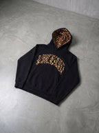 Leopard trim hoodie in black, laid flat on concrete floor