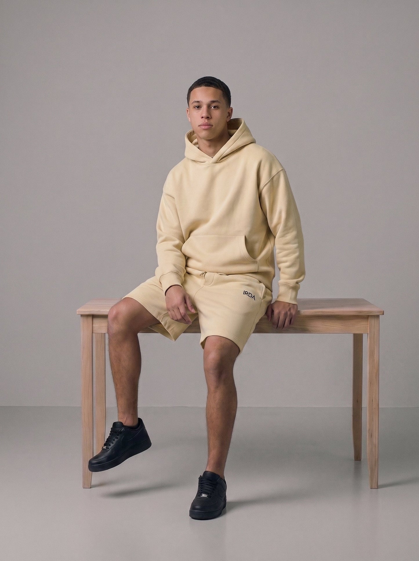Men's oversized fleece hoodie and shorts set in cream, full body on bench